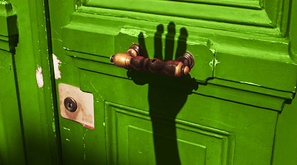 green door with shadow of an arm and hand reaching toward the knob to open it
