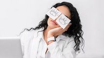 Woman sitting in front of laptop computer with drawings of eyes covering her real eyes